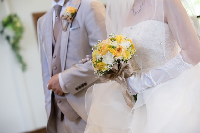 結婚式でバージンロードを歩いているカップルの首下写真。目的が結婚であることを明示しています。